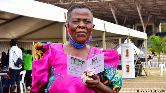 A woman in pink holds up a Ugandan vaccine certificate