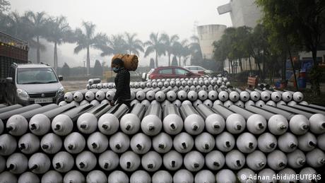 A worker carries an oxygen cylinder past a row of cylinders in Delhi
