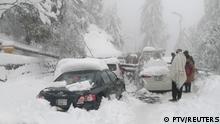 People stand next to cars stuck under fallen trees on a snowy road, in Murree, northeast of Islamabad, Pakistan in this still image taken from a video January 8, 2022. PTV/REUTERS TV via REUTERS THIS IMAGE HAS BEEN SUPPLIED BY A THIRD PARTY.
