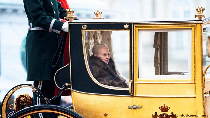Queen Margrethe II of Denmark sitting in a yellow carriage. 