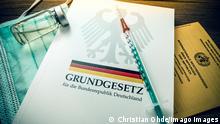 Jeringuilla de vacunación sobre la Constitución alemana y un cuaderno de registro de vacunación.