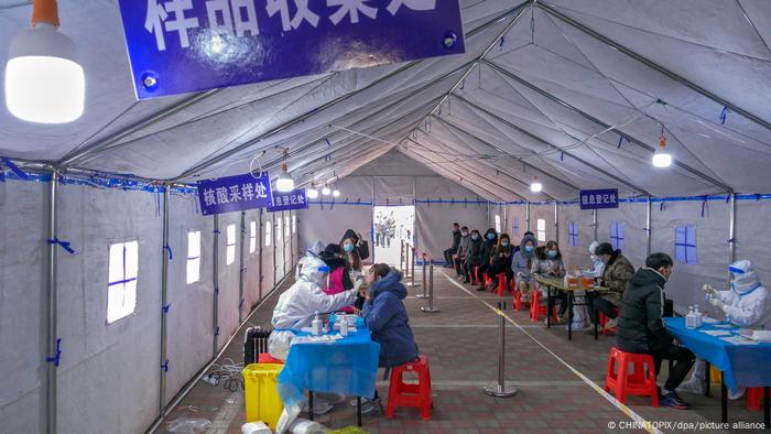 En China, una gran carpa blanca, filas de mesas con personas sentadas a cada lado.