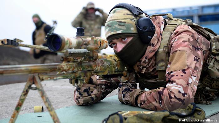 A soldier looks into a sniper rifle scope