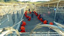 GUANTANAMO BAY, CUBA - JANUARY 11: In this handout photo provided by the U.S. Navy, U.S. Military Police guard Taliban and al Qaeda detainees in orange jumpsuits January 11, 2002 in a holding area at Camp X-Ray at Naval Base Guantanamo Bay, Cuba during in-processing to the temporary detention facility. The detainees will be given a basic physical exam by a doctor, to include a chest x-ray and blood samples drawn to assess their health, the military said. The U.S. Department of Defense released the photo January 18, 2002. (Photo by Petty Officer 1st class Shane T. McCoy/U.S. Navy via Getty Images)