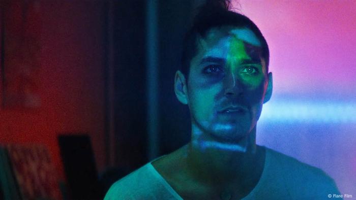 Filmstill I EVERYTHING WILL CHANGE : Ein Mann schaut auf eine Leinwand, die sich in seinem Gesicht reflektiert 