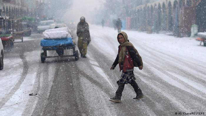 A girl wearing a scarf crosses a street in the snow in Bamiyan, Afghanistan, 22.12.2021