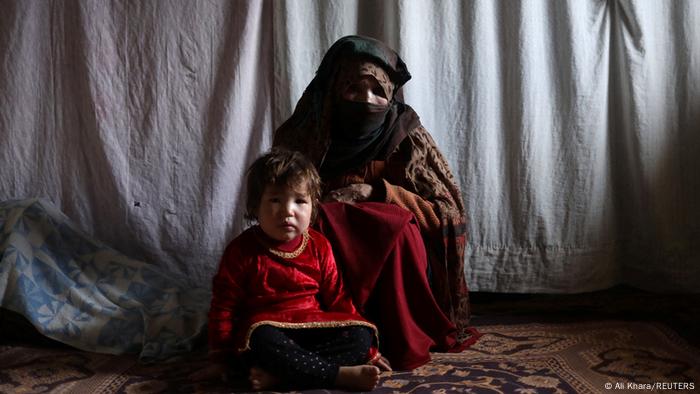 Kubra, 57, and her grandson sit in their meager accommodation and look at the camera, Bamiyan, Afghanistan, 22.12.2021