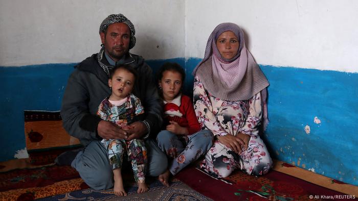 Market porter Sayed Yassin Mosawi, 31 sits with his wife and two young children in his sparse hut in Bamiyan, Afghanistan. 22 December 2021
