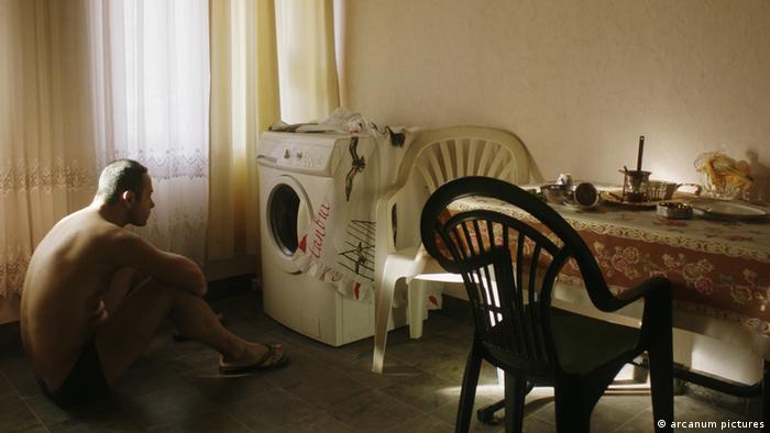 Filmstill von Return: Ein Man sitzt in Unterhose vor einer Waschmaschine.
