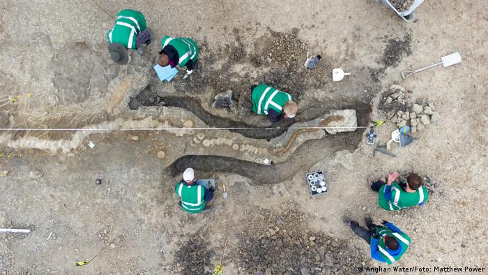 Aerial view of six people in green jackets digging in the ground .