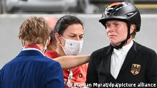 Fünfkämpferin Annika Schleu schaut nach dem Springreiten bei den Olympischen Spielen in Tokio traurig, während Bundestrainerin Kim Raisner die Startnummer von Schleus Rücken entfernt