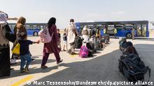 Frauen mit Kopftüchern, Kinder und Männer stehen in einer Warteschlange vor mehreren Bussen