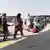 Frauen mit Kopftüchern, Kinder und Männer stehen in einer Warteschlange vor mehreren Bussen