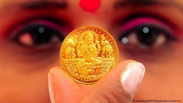 Женщина держит золотую монету с изображением индийской богини Лакшми