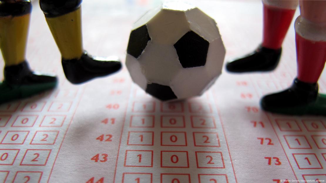 Bir bahis kuponu üzerinde yer alan oyuncak top ve iki futbolcu figürü Bir bahis kuponu üzerinde yer alan oyuncak top ve iki futbolcu figürü