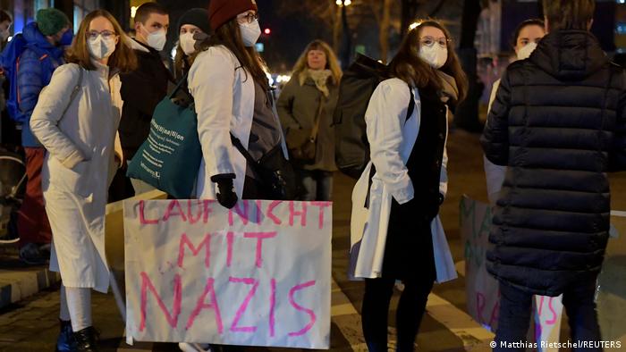 A counterprotester in medical garb holding a sign that reads 'don't walk with Nazis'