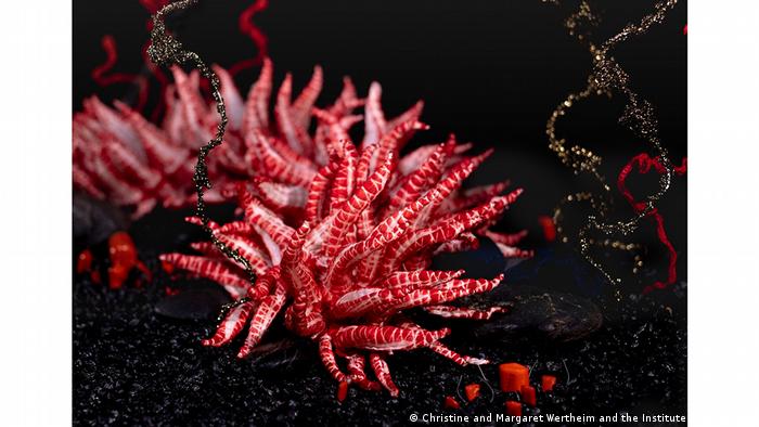 Eine Figur, die an rote und weiße Korallen und schwarze Spiralen erinnert, die an Filamente aus einem Teil des Crochet Coral Reef Project erinnern