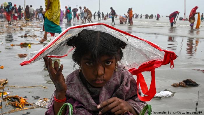 A child covers her head with a plastic bag to shelter from the rain on the backdrop of Hindu pilgrims gathered at the banks of Ganges.