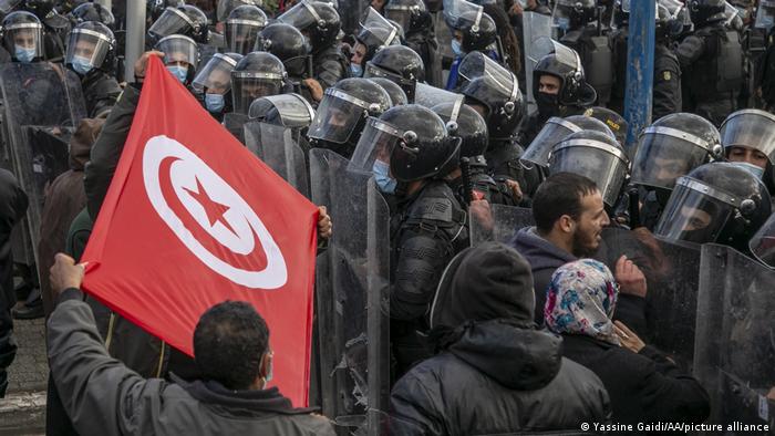 Protesters hold the Tunisian flag as they stand in front of security forces
