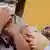 Criança usando máscara leva as mãos à boca enquanto uma enfermeira, também de máscara, segura o ombro dela e espeta uma agulha contendo imunizante.