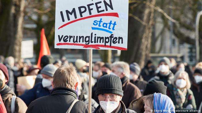 Protester holds a sign that reads, in German: Vaccinate rather than vilify!