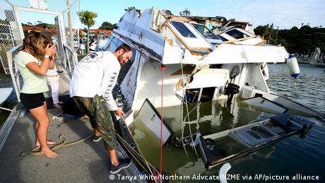 A couple look at a damaged boat at a marina in New Zealand