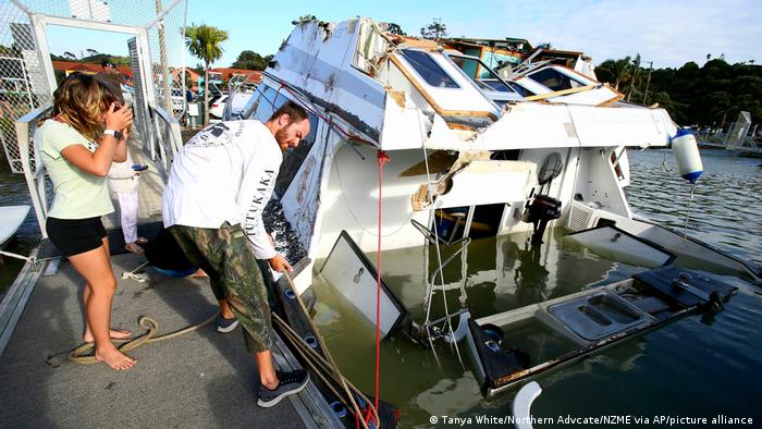A couple look at a damaged boat at a marina in New Zealand