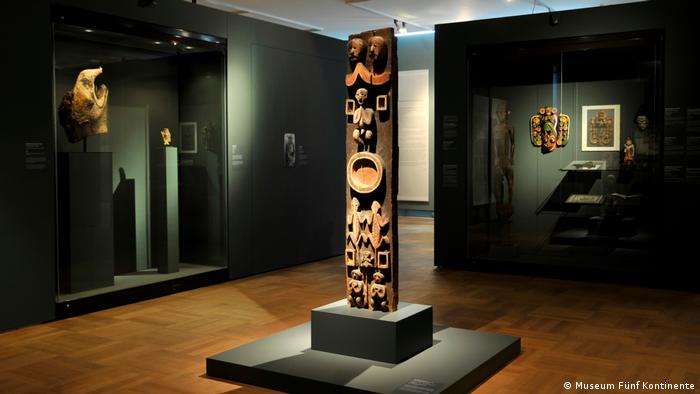 Blick in die Afrika-Sammlung des Museums Fünf Kontinente in München. IN der Mitte sieht man den sogenannten Blauer-Reiter-Pfosten, ein hochformatiger Holzbalken, der mit Schnitzereien, die Tiere und Menschen zeigen, verziert ist. 