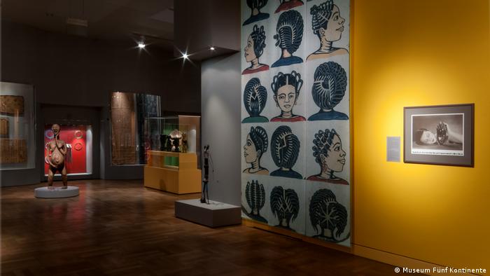 Blick in die Ausstellung des Museum Fünf Kontinente in München. Man sieht eine Wand mit gemalten Portraits einer afrikanischen Frau, der Fokus liegt auf ihren verschiedenen Frisuren. 