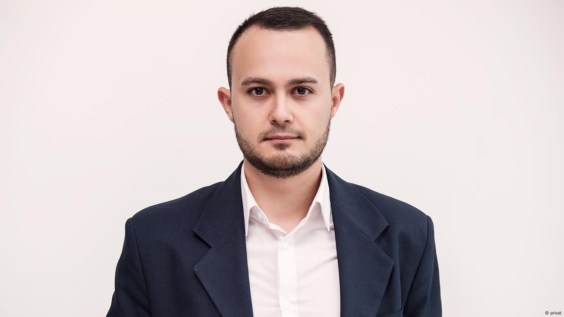 Foto de Velkov. Ele é jovem veste camisa branca e blazer escuro.