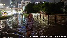 A man wades through flood waters in Jakarta, traffic and the illuminated city can be seen behind him 