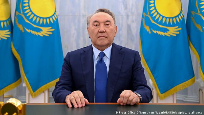 Nursultan Nazarbayev, the former leader of Kazakhstan, seated at a desk, flanked by Kazakh flags