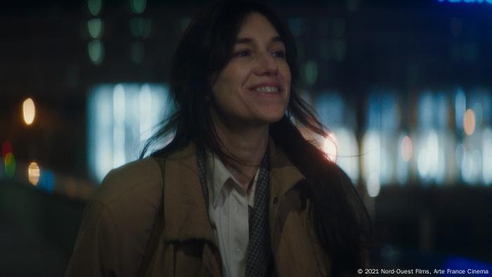Charlotte Gainsbourg tertawa di depan lampu berkabut di latar belakang - adegan dari Les Passers de la nuit