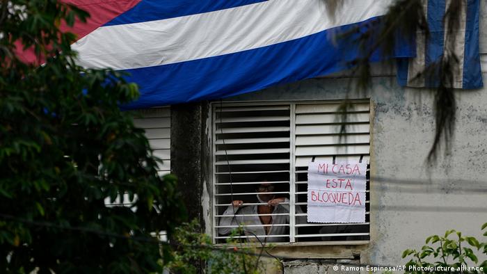 Kuba: Yunior Garcia hinter den Lamellen am Fenster, daneben ein Schild, über ihm an der Hauswand eine riesige kubanische Flagge