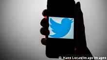 A hand holding up a cellphone displaying the Twitter logo 