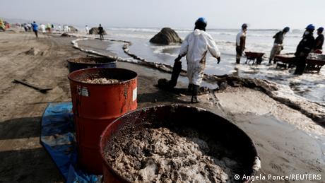 Trabajadores con trajes especiales retiran el vertido petrolero que afecta playas de la provincia peruana de El Callao.