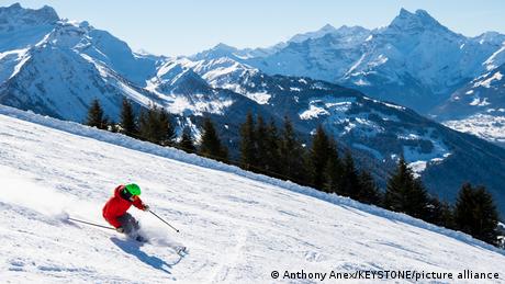 A single skier going down a snowy slope with blue skies and the Alps in the background in the ski resort Les Chaux in Switzerland.