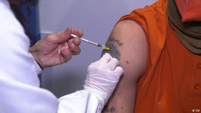A person injects a vaccine into the upper arm of another (no faces visible)