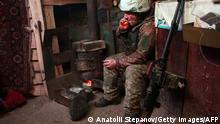 TOPSHOT - An Ukrainian Military Forces serviceman smokes in a dugout, as he and a cat sit near a wood burner on the frontline with the Russia-backed separatists near Zolote village, in the eastern Lugansk region, on January 21, 2022. - Ukraine's Foreign Minister Dmytro Kuleba on January 22, 2022, slammed Germany for its refusal to supply weapons to Kyiv, urging Berlin to stop undermining unity and encouraging Vladimir Putin amid fears of a Russian invasion. (Photo by Anatolii STEPANOV / AFP) (Photo by ANATOLII STEPANOV/AFP via Getty Images)