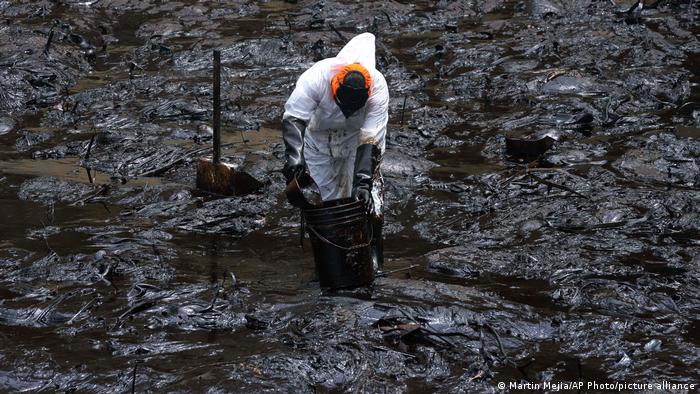 An emergency worker in a white biosecurity suit cleans up a beach affected by the La Pampilla oil spill