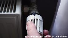 hand turning off thermostat on radiator to save energy due to increasing heating costs