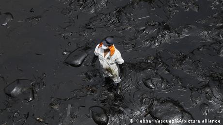 A cleanup worker stands in a thick layer of oil on a beach in Lima, Peru.