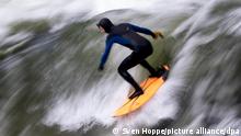 Ein Mann reitet auf der Eisbachwelle im Englischen Garten. Die künstliche Welle gilt das ganze Jahr über als ein beliebter Hotspot für Surfer und Zuschauer.