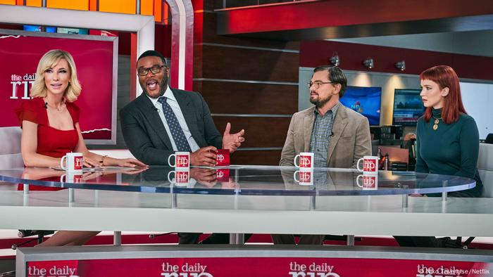 four people seated around a table during filming for a TV show