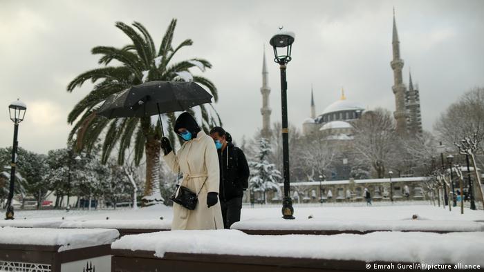 Backdropped by the historical Sultan Ahmed or Blue Mosque, people walk in the snow at Istanbul