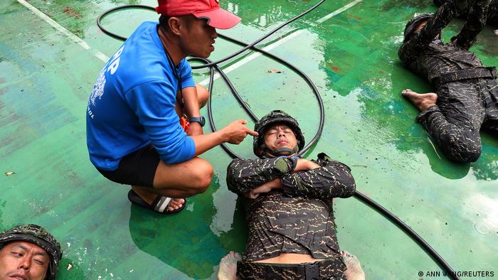 Seorang pelatih ARP memarahi seorang peserta pelatihan dengan perlengkapan tempur saat ia berbaring di samping peserta pelatihan lainnya di tanah basah 