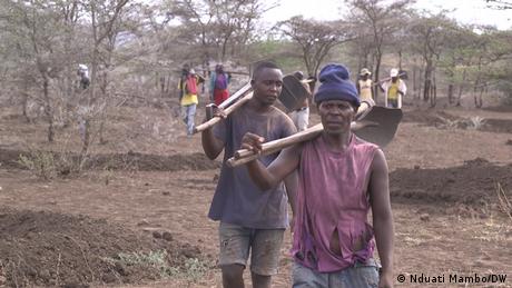 Two men in the Arusha region of Tanzania carry spades on their shoulders.