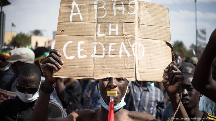 A man holds a sign saying 'Down with ECOWAS' in French
