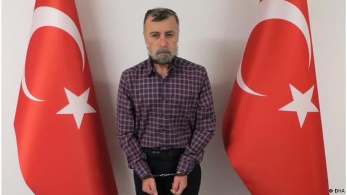 Nuri Bozkir stands handcuffed between two Turkish flags