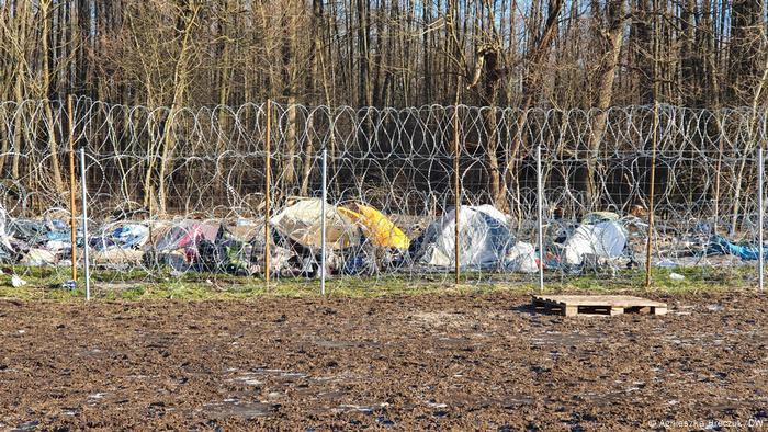 The remains of a makeshift camp near a razor wire fence